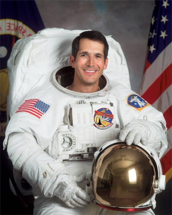 A person wearing an astronaut uniform smiles.